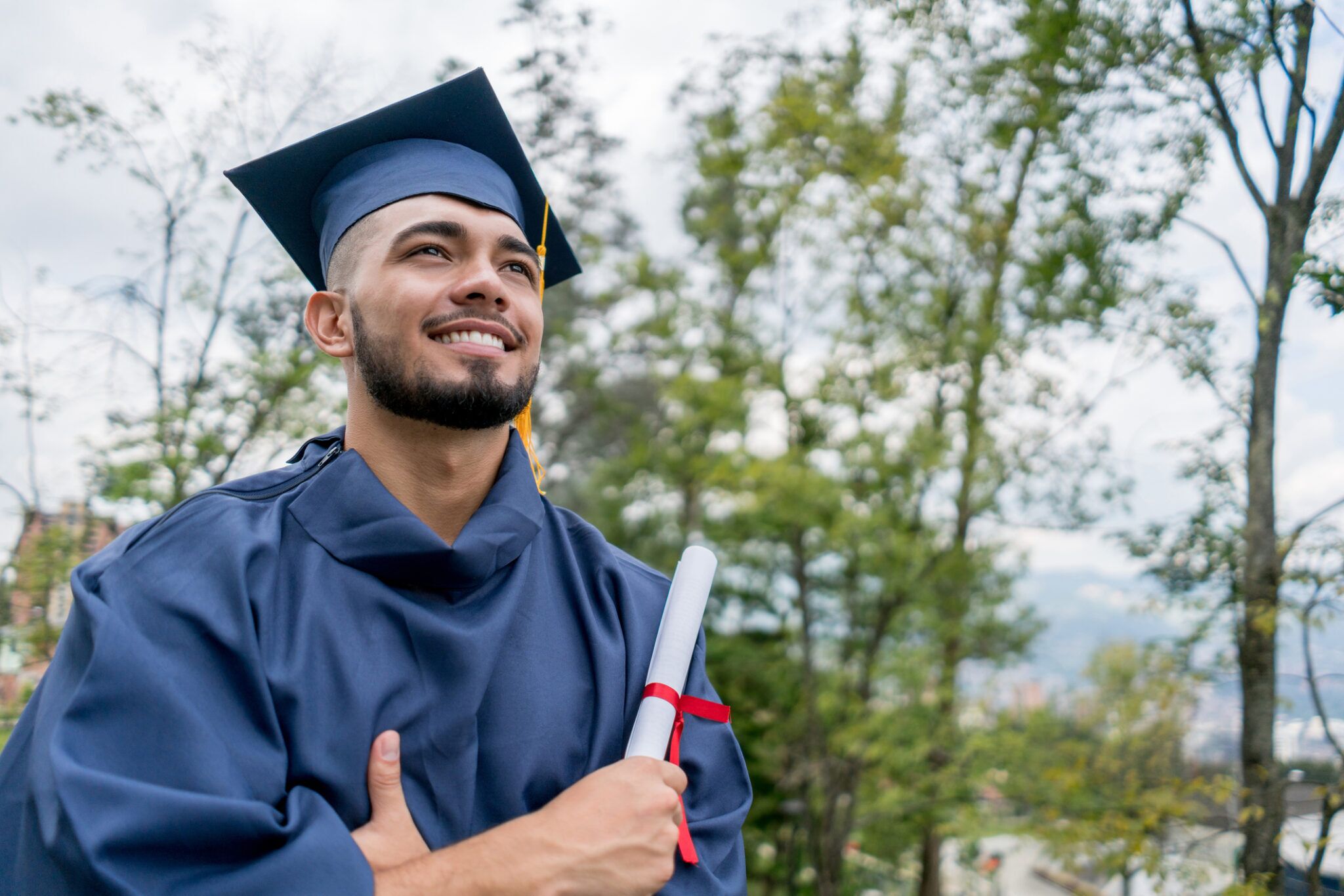 Latin american young man very happy after receiving his diploma looking away with arms crossed