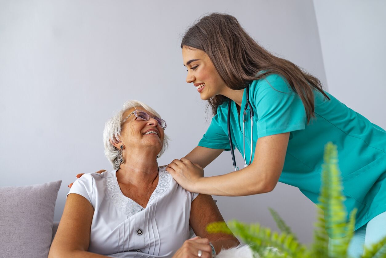 Young caregiver and senior woman laughing together while sitting on sofa